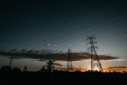 A landscape shot of metallic transmission towers with powerlines connecting them during sunset