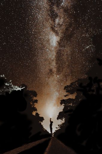 A vertical shot of a person standing on the road with the starry night sky in the background