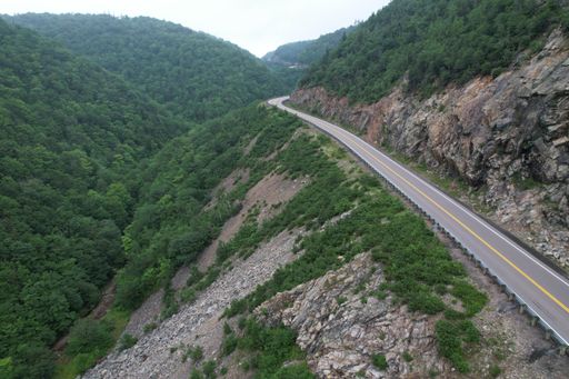 An aerial shot of mountain road surrounded by dense forest in daylight