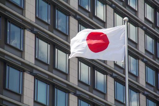 A low angle shot of the flag of Japan waving in the wind in front of the buildings on a sunny day