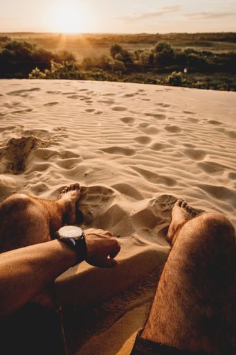 A vertical shot of a sandy area with a man's legs and left hand visible in the shot during daytime