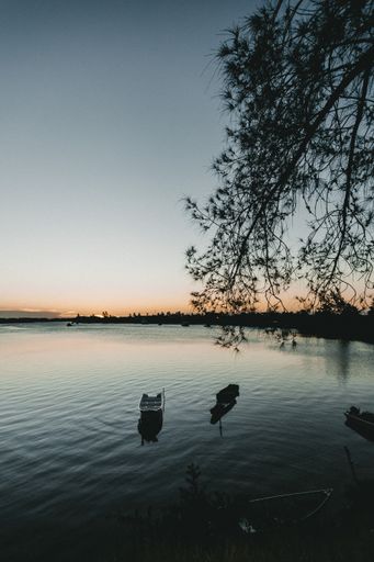 A vertical shot of a serene lake with four rowboats on it during sunset