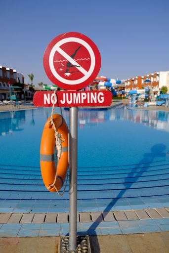 A vertical shot of a "No jumping" sign and a lifebuoy near the swimming pool