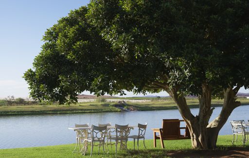 A beautiful shot of a wooden bench and white table with chairs at the riverside