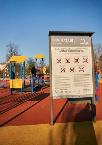 A vertical shot of an information sign showing different rules next to playground in the Rataje park on a sunny day