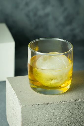 A vertical shot of a cup of single malt scotch whisky with an ice cube on a concrete brick