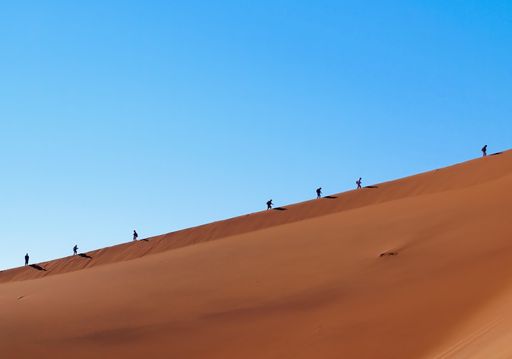 An aerial shot of people hiking on beautiful orange namibian sand dunes on a sunset day