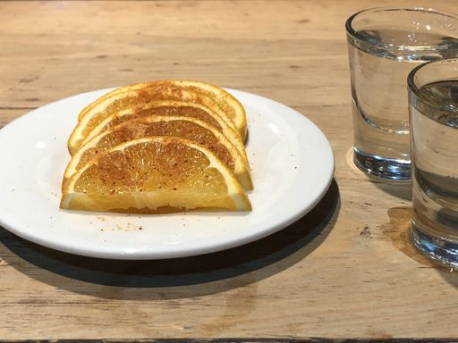 A closeup of seasoned slices of orange in a plate on the table with tequila shots