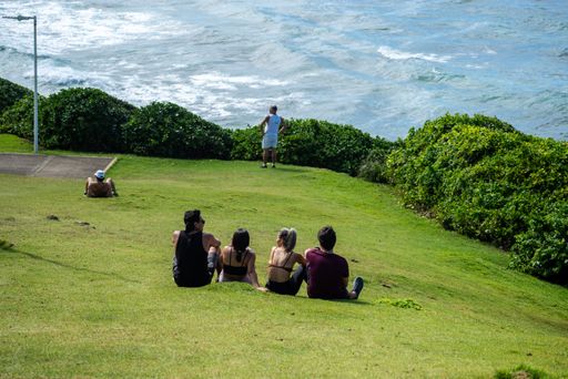 The people sitting on the grass enjoying the landscape of Farol da Barra beach in Salvador, Bahia, Brazil