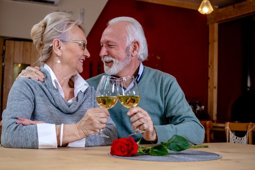 A mature romantic couple of caucasian man and woman sit in a restaurant. Seniors in love, looking at each other, toasting and clinking glasses with wi