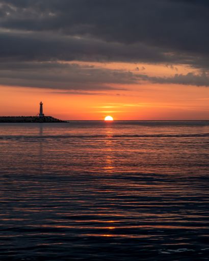 A vertical shot of a sea with a lighthouse in the background at sunset