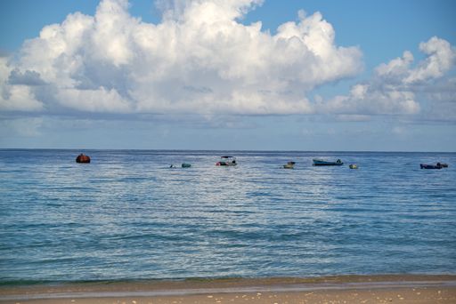 A scenic view of a sandy shoreline under the cloudy sky with the ships in the water