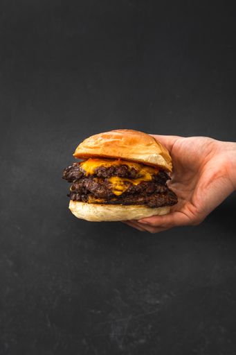 A vertical shot of a hand holding a juicy triple burger with cheese on a black background