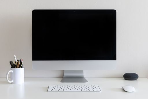 A work desk with a computer, a cup with pens and pencils against a white wall