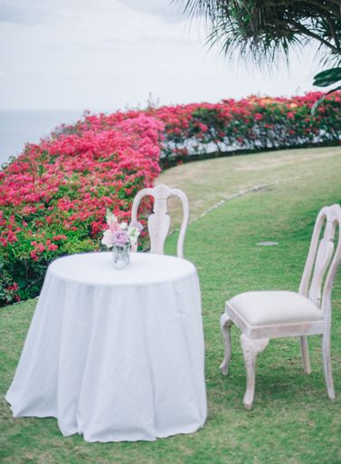 A small round table with two white chairs in a garden with beautiful red roses on a sunny day