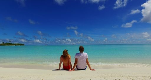 A rear view of a couple sitting on the sandy beach of the ocean in Rasdhoo Island, the Maldives