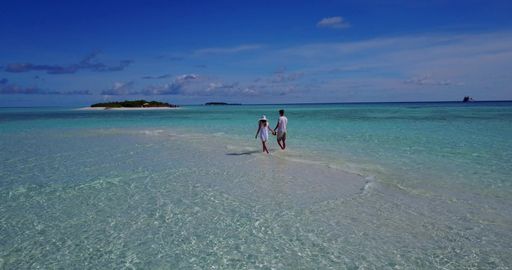 A panoramic view of a beautiful loving couple walking at the beach of the ocean in Rasdhoo Island, the Maldives