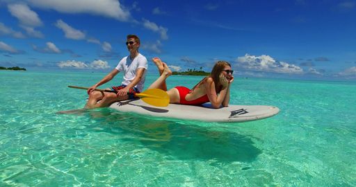 A view of a loving happy couple sitting on the surf board in Rasdhoo Island, the Maldives