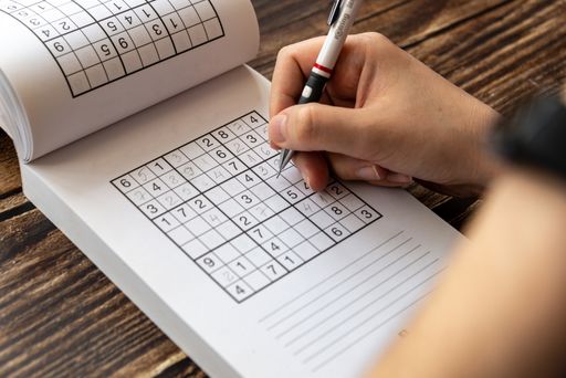A person solving a sudoku puzzle on a wooden table