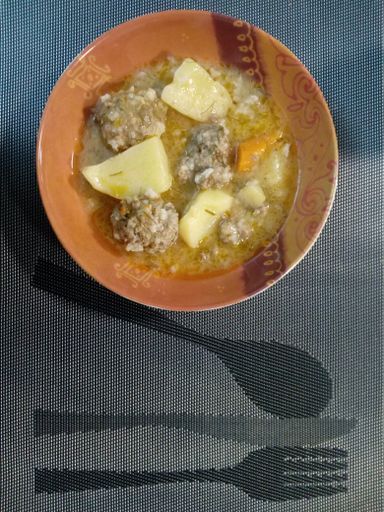 A vertical shot of soup of meatballs with potato and squash in a bowl on a placemat