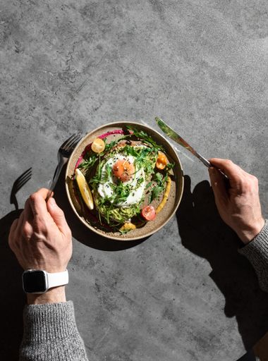 A top view of a male hands with fork and knife to eat omelette with greens, cherries and lemon slice