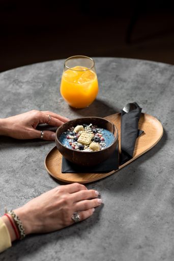 A vertical shot of female hands on the table with a cup of orange juice and a bowl of smoothie