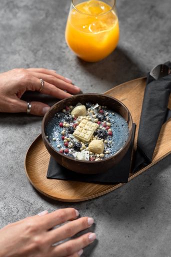 A vertical shot of female hands on the table with a cup of orange juice and a bowl of smoothie
