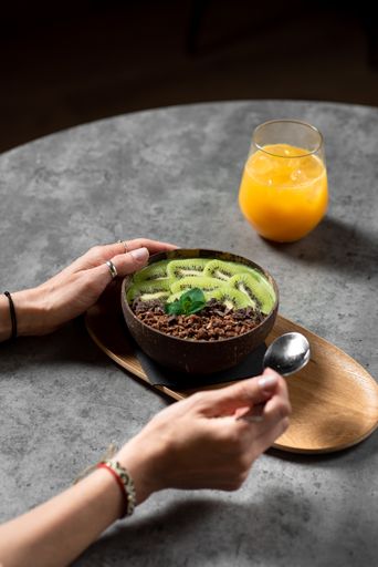 A vertical shot of female hands eating tasty oatmeal with kiwi and chocolate on the table with a cup of orange juice