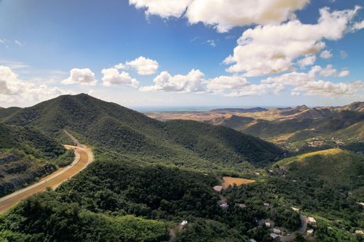 A panoramic view of green hills, cloudy sky and highway through forest