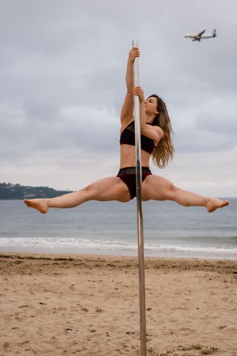 A vertical shot of a young female dancing on a pole with a plane in the sky on Hendaya beach, France