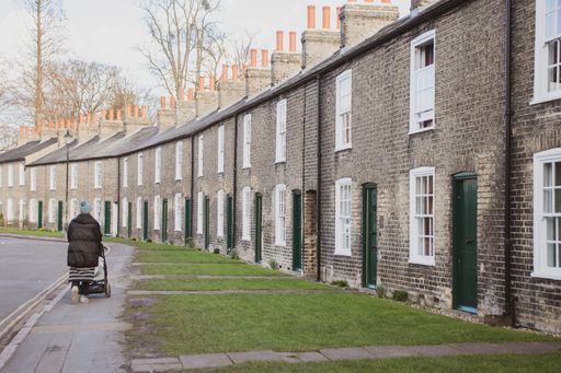 A woman with a stroller walking along the sidewalk next to the houses in Cambridge, England