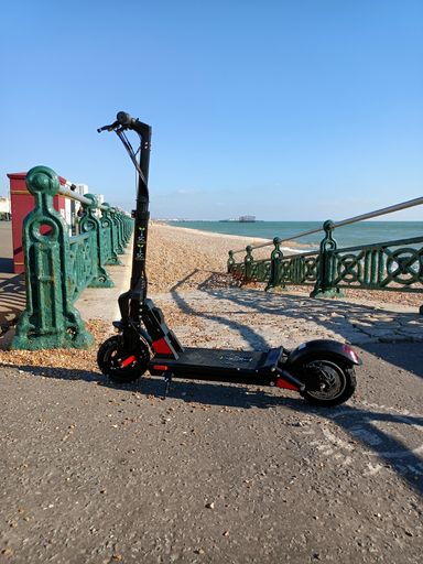 A closeup shot of a Nitro black Electric Scooter in the street with green metal fence with blue sunny sky in Brighton, UK