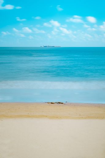 A vertical shot of the blue sky over the sea captured from the sandy beach in summer