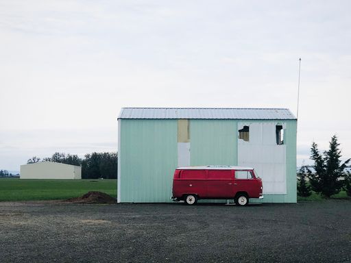 A beautiful shot of a red van in front of a white rural barn with trees against a light bright sky