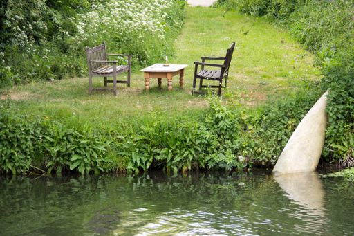 Two chairs with a table in a park covered in greenery surrounded by a lake at daytime