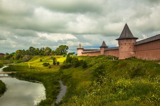 A beautiful shot of castle walls on a grassy hill near a river under a cloudy sky