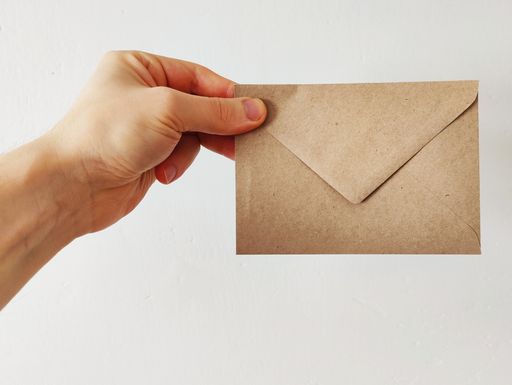 A hand holding a paper envelope against the white wall