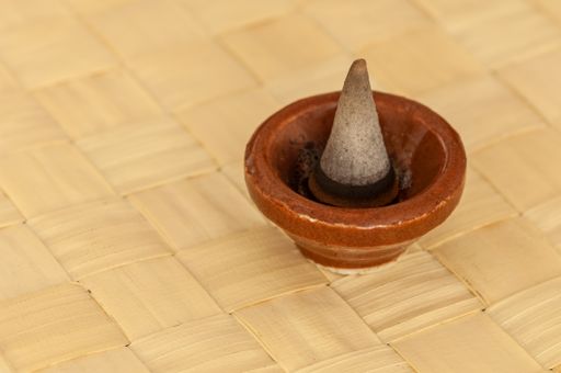 A closeup of a conic-shaped incense in a small terracotta bowl