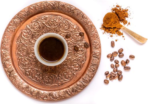 A cup of dark coffee on a golden tray with patters and some coffee beans nearby