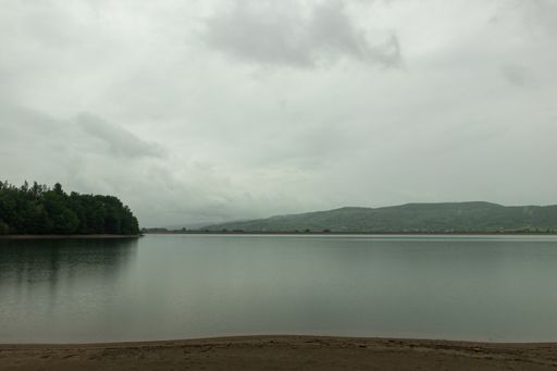 A beautiful scenery of a lake surrounded by greenery under dark storm clouds