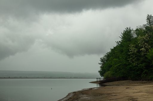 A beautiful scenery of a lake surrounded by greenery under dark storm clouds