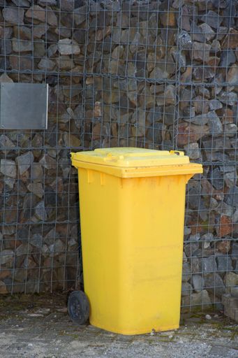 A vertical shot of a yellow trash can on the street