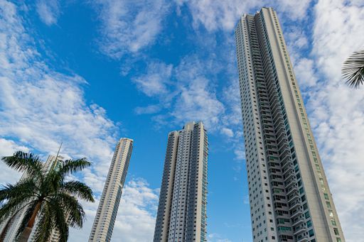 A bottom shot of some skyscrapers in the background of a cloudy sky.
