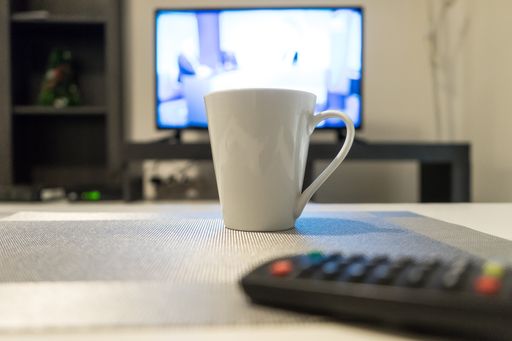 The close-up selective focus shot of a white mug with a tv in the back