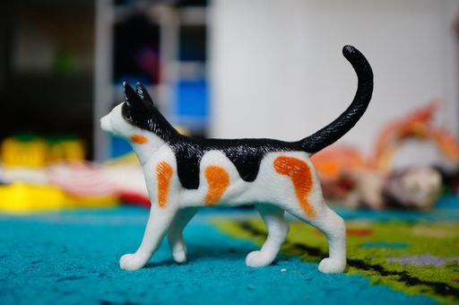 A closeup of a toy white cat with black and red spots on a blue carpet under the lights