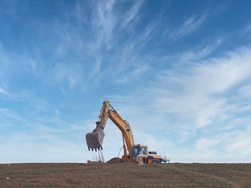 a photo of excavator working moving dirt and loading onto a truck with blue sky and clouds