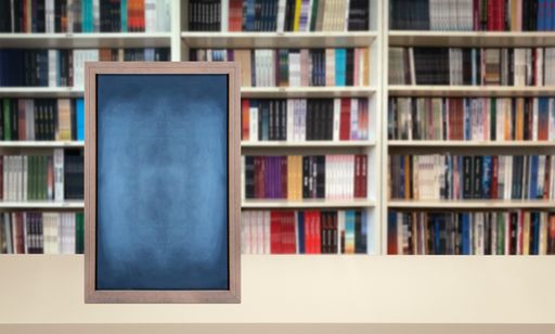 An empty chalkboard is prominently displayed in a room with a bookshelf in the background