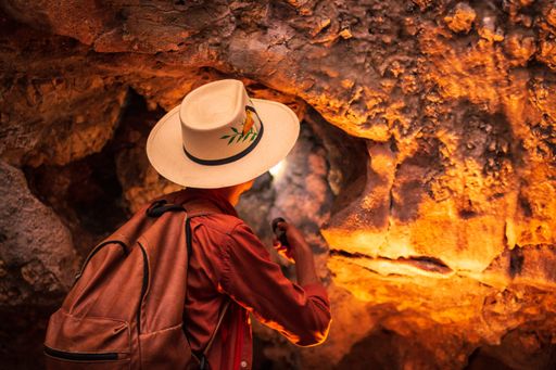 A horizontal shot of a female with a hat walking with a flashlight in the cave