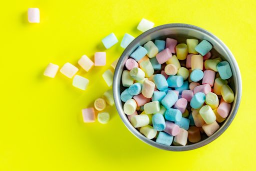 A high angle shot of a metal bowl with sweet colorful marshmallows on a yellow surface
