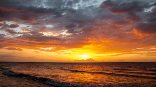 A wide shot of the breathtaking sunset behind the clouds reflected in the beautiful sea in the evening